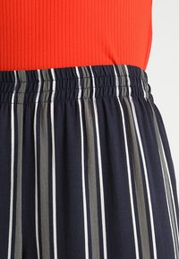 Närbild av en midja i marinblå byxor med vertikala gråa och vita ränder och ett elastiskt midjeband, matchat med en röd ribbad topp.