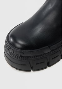 Svart ankelstøvel med glatt skinnoverdel, tykk svart platåsåle og teksturerte detaljer på siden. Har preget logo.