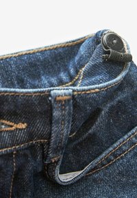 Jeans de mezclilla azul con una cinturilla ancha, cierre de botón negro, costuras visibles en un tono beige en contraste y un borde doblado para mayor textura.