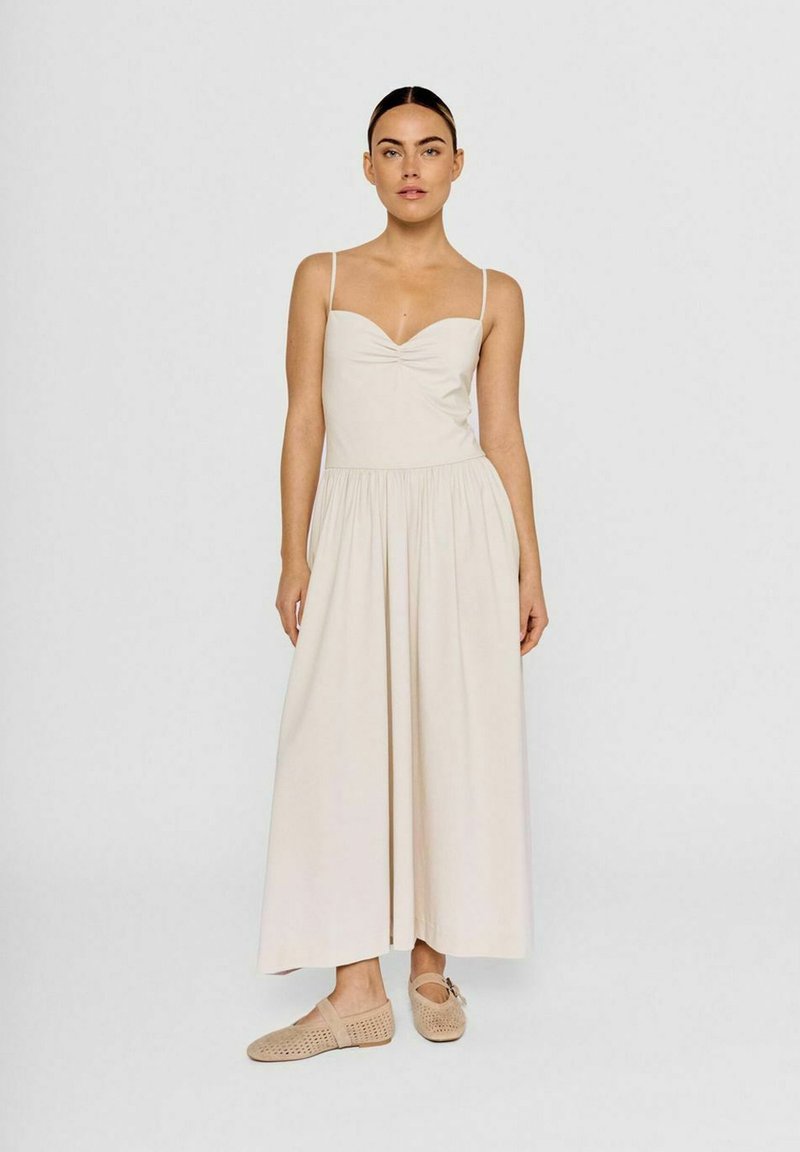 Beige midi-kjole med tynde stropper, samlet bustdetalje, flagrende skørt og blød tekstur, parret med lyse beige slip-on sko.
