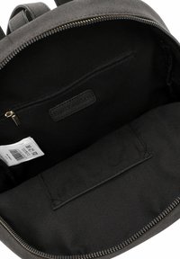 Interno di uno zaino in tessuto nero con una tasca con cerniera e un'etichetta patch; texture liscia e forma arrotondata con dettagli in metallo dorato.