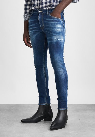 Tætsiddende, mørkeblå jeans med slidte accenter, ledsaget af sorte ankelstøvler med elastiske sidepanele. Struktureret denim-overflade.