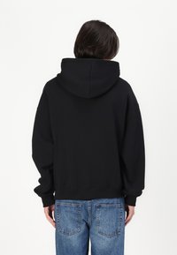 Svart hettegenser med avslappet passform, med teksturert stoff, senket skulder og ribbestrikkede mansjetter. Brukt med lys blå denimjeans.