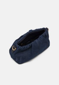 Sac en denim marine avec un haut froncé, de forme ovale et des accessoires en métal doré. L'intérieur présente une doublure noire et une étiquette de marque.