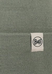 Gorro de punto verde con una textura suave, que presenta una etiqueta blanca con el logo negro de "Buff". Puño doblado en la parte inferior.