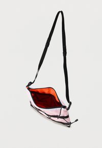 Μικρή ροζ τσαντούλα ώμου με μαύρο ρυθμιζόμενο λουράκι, πορτοκαλί εσωτερικό, μαύρο φερμουάρ και εξωτερική μαύρη ελαστική λεπτομέρεια κορδονιού.