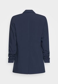 Marinblå kavaj med skräddarsydd design, strukturerade axlar och samlade ärmdetaljer. Slät textur och en enda ventil bak.