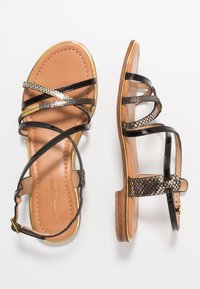 Sandali neri con cinturini, dettagli metallici, soletta in pelle beige, rifiniture dorate lungo i bordi e suole piatte. Cinturini in tessuto flessibile.