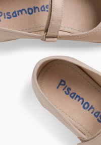 Pantofii slip-on din material bej cu brățară ajustabilă, vârf rotunjit și logo albastru "Pisamonas" pe interior. Textură moale și design minimal.