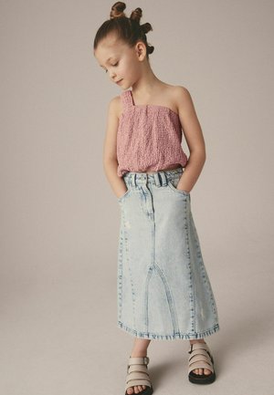 Rosa texturerad topp med en enda rem, i kombination med en ljusblå denimkjol med sidofickor och synliga sömnadsdetaljer. Svarta sandaler.