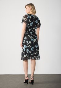 Floral dress in black chiffon, featuring light blue and gray flowers, flutter sleeves, and a flared hem. Black heeled sandals complete the look.
