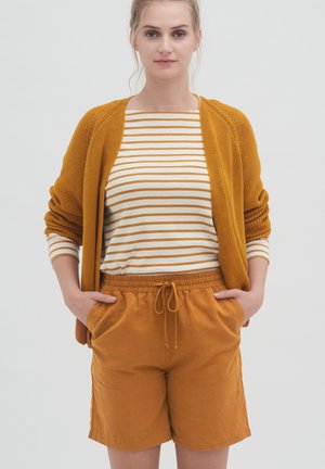Strickcardigan in Senfgelb, gestreiftes Langarmshirt in Creme und Orange sowie kurze Shorts mit Kordelzug in passendem Senfgelb. Lockere Passform mit Taschen.