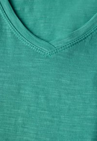 Teal V-ringad T-shirt i mjukt tyg, med en slät yta och subtilt melerat mönster. Har en sömnad vid halsringningen och en avslappnad passform.