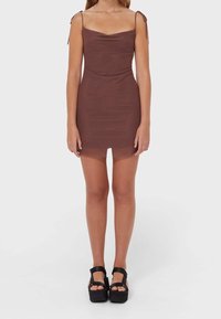 Brun klänning med smala axelband, texturerad tyg och rundad halsringning, matchad med svarta platåsandaler.