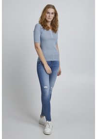 Gaiši zils ribota īsajiem piedurknēm tops ar pogu detaļu, savienots ar nodilusiem ziliem šaurajām biksēm un baltiem sporta apaviem. Vienkārša, ikdienišķa apģērba izvēle.