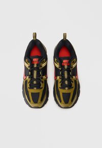 Par de sapatilhas Nike Vomero 5 nas cores preto, verde-oliva e vermelho, com parte superior em malha e abas de puxar, vistas de cima sobre um fundo branco.