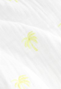 Tissu blanc avec de petits palmiers brodés jaune clair dispersés à la surface, montrant des plis doux dans le matériau.