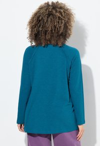 Maglietta a maniche lunghe in tessuto teal, con una vestibilità rilassata e maniche raglan. Texture liscia con dettagli di cucitura minimi sulle spalle.