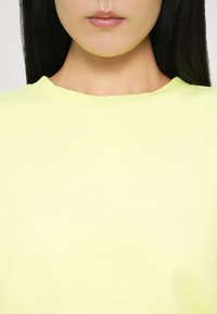 Limegrønn bomull T-skjorte med rund hals, med preget tekst "STIEGLITZ" på brystet. Glatt tekstur, avslappet passform.