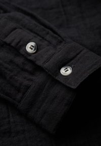 Zwarte button-up shirt met een textuurstof. Bevat zilveren knopen bij de manchetten en een gestructureerde kraag met zichtbare stikdetails.