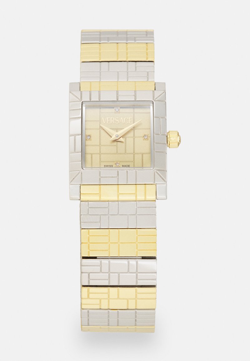 Kvartskellaga, millel on ruudukujuline kullast kellapaneel, teemantaccentidega, hõbedast ja kullast omavahel põimuv metallist rihm, millel on tekstuurilised mustrid. Versace bränding on nähtav.