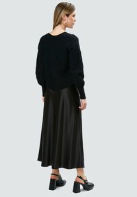 Maglione nero lavorato a maglia con maniche a palloncino testurizzate, abbinato a una gonna nera di satin fluida e scarpe nere con tacco largo.