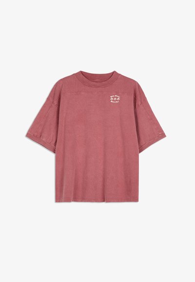 Př oversized tričko s krátkým rukávem v barvě prachové růže, vyrobené z měkké bavlny s jemnou grafikou na hrudi a uvolněným střihem.
