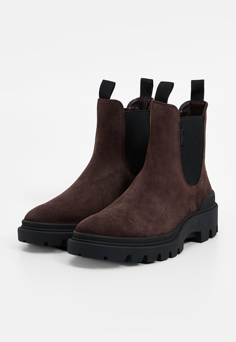 Bottines Chelsea en suède marron avec des panneaux élastiques sur les côtés, des tirettes et des semelles en caoutchouc noir épaisses, présentant une finition texturée et un design élégant.