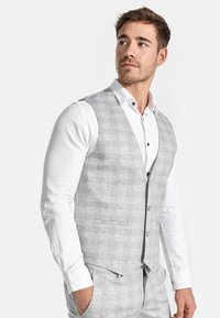 Graue karierte Weste aus strukturierter Stoff, mit V-Ausschnitt, Seitentaschen und Knopfverschluss, kombiniert mit einem weißen Langarmhemd.