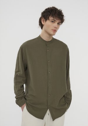 Camicia verde oliva con bottoni, colletto alla coreana, maniche lunghe, texture sottile e design dell'orlo curvo; presenta bottoni marroni.