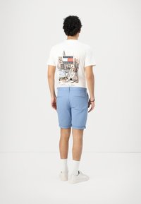 Camiseta blanca de manga corta con un estampado gráfico en la parte de atrás que presenta una escena de la ciudad. Pantalones cortos de color azul claro con dobladillo enrollado y bolsillos traseros.