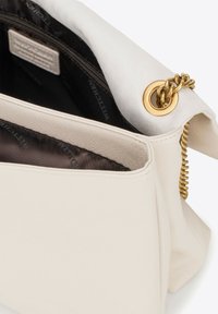 Sac en cuir blanc avec une accent en chaîne dorée, doté d'une fermeture zippée, d'une doublure intérieure texturée et d'un design doux et structuré.