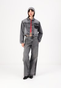 Kuttet grå denimjakke med frontlommer, kombinert med høyt liv og vide grå jeans. Modellen har på seg en rød topp og en grå lue.