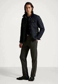 Tamsiai mėlyna dygsniuota striukė su juodu apykakliu, dvi priekinės kišenės, dėvima virš juodos marškinių. Prie to priderinti pilki kelnės ir juodi batai.