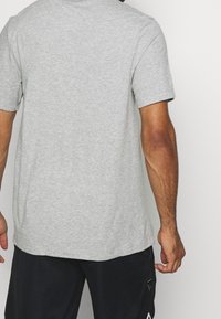 Camiseta gris de manga corta hecha de una tela suave y transpirable, con un corte relajado y escote redondeado, costuras visibles en el dobladillo.