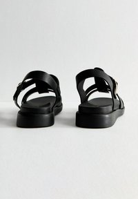 Svarta lädersandaler med platt sula, med flera remmar och en spänneaccent. Öppen häl-design och slät yta.