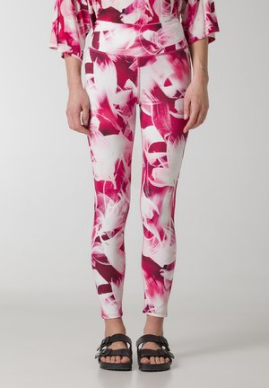 Leggings ajustados en un patrón floral rosa y blanco, hechos de un material elástico con una cinturilla alta. Se llevan sandalias negras.