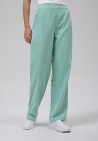 Lyse mintgrønne bukser med en glat tekstur, bred bendesign og skarpe linjer, parret med hvide slip-on sko.