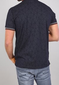 Laivastonsininen poolopaita, jossa on geometrinen kuvio, lyhyet hihat, joissa punaiset, valkoiset ja vihreät raidat hihansuihin, puuvillasekoitemateriaalia.