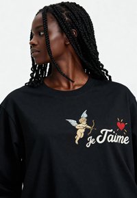 T-shirt en coton noir avec un dessin brodé d'un cupidon ailé tenant un arc, accompagné du texte "je t'aime" en blanc, à côté d'un cœur rouge.