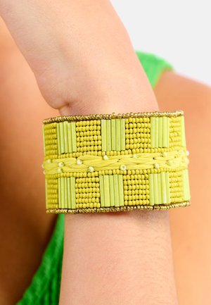 Bracelet jaune en perles comprenant diverses formes et textures, incluant de petites perles rondes et des pièces rectangulaires, avec des accents dorés.