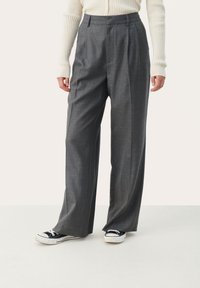 Grijze op maat gemaakte broek met een hoge taille, brede pijpen en voorplooien, gecombineerd met zwarte sneakers. Glad materiaal met een subtiele textuur.