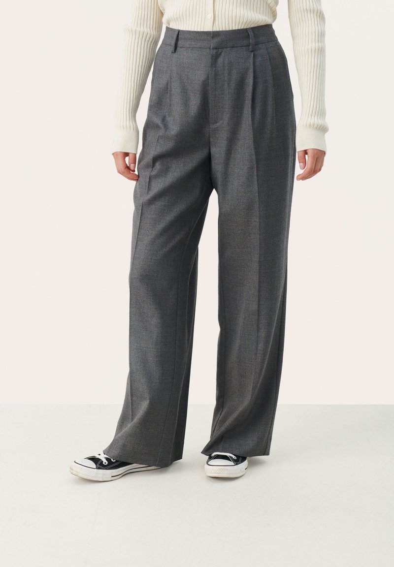 Grijze op maat gemaakte broek met een hoge taille, brede pijpen en voorplooien, gecombineerd met zwarte sneakers. Glad materiaal met een subtiele textuur.