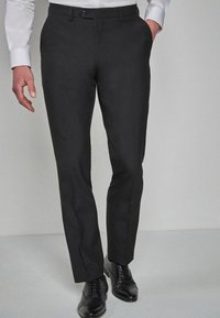 Pantaloni negri din stofă cu croi slim, confecționați dintr-un material neted, având buzunare laterale, față plată și închidere cu nasture, asortați cu pantofi negri.