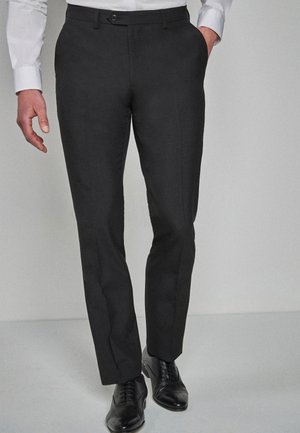 Pantaloni negri din stofă cu croi slim, confecționați dintr-un material neted, având buzunare laterale, față plată și închidere cu nasture, asortați cu pantofi negri.
