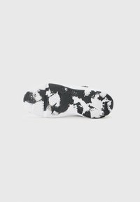 Semelle de chaussure de sport en noir et blanc, en caoutchouc texturé avec un motif de taches distinct et des motifs de semelle variés pour une meilleure adhérence.