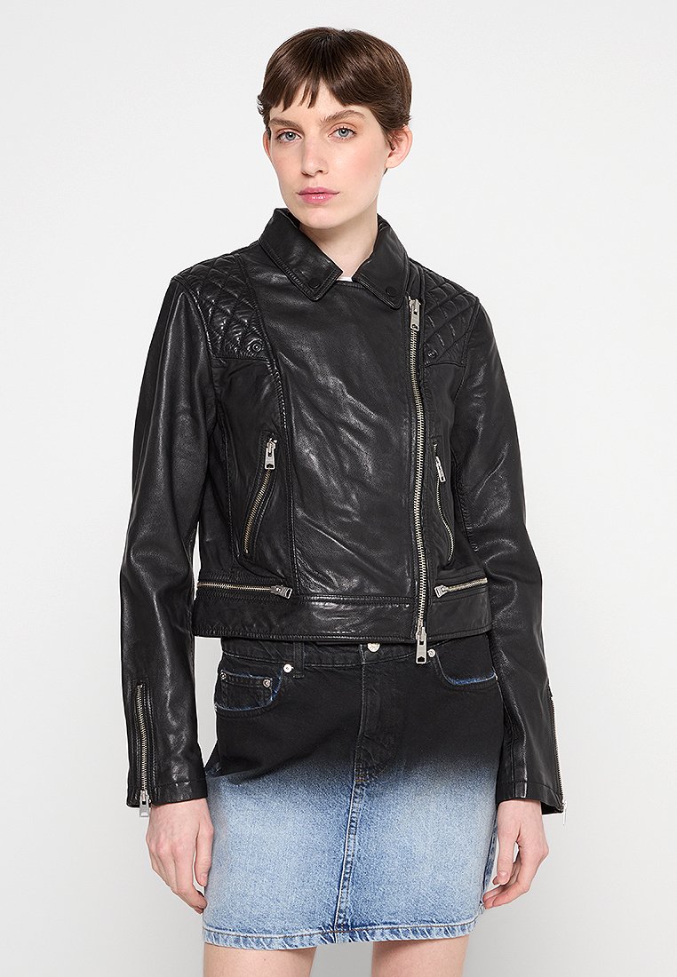 Giubbotto in pelle nera con dettagli trapuntati sulle spalle, chiusura a zip asimmetrica e due tasche laterali con zip, indossato sopra una gonna di jeans.