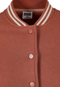 Bordo bomber jakna z rebrastim ovratnikom s belimi črtami. Sprednji gumbi in mehka tekstura blaga. Oznaka pravi "Urban Classics, XS."