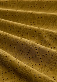 Olivengrön textrad tyg med utskurna mönster, med en diamantdynamik och små hål genom hela ytan, draperad i mjuka veck.