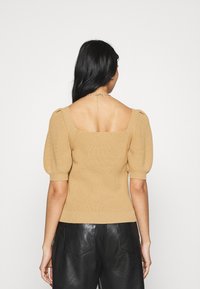 Top de punto marrón con mangas cortas abullonadas, escote cuadrado, textura acanalada y diseño ajustado, combinado con pantalones de piel negra.